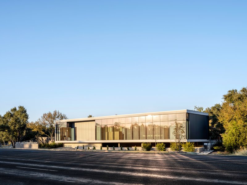 Long street view of the translucent glazed facade glowing between dark metal end volumes at twilight