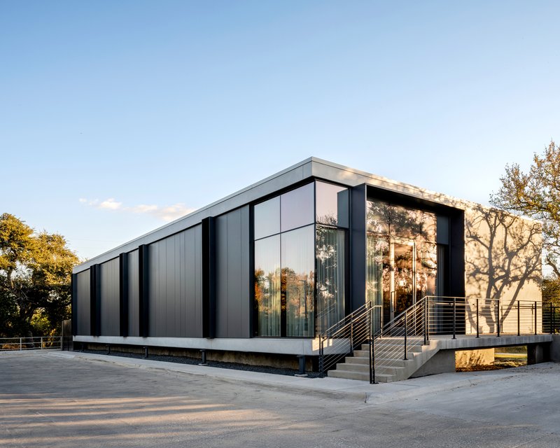 Corner view of the elevated volume with vertical metal cladding and concrete access stairs at sunset