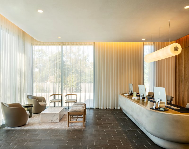 Reception desk with curved front and herringbone tile floor beneath sheer curtains and suspended pendant light