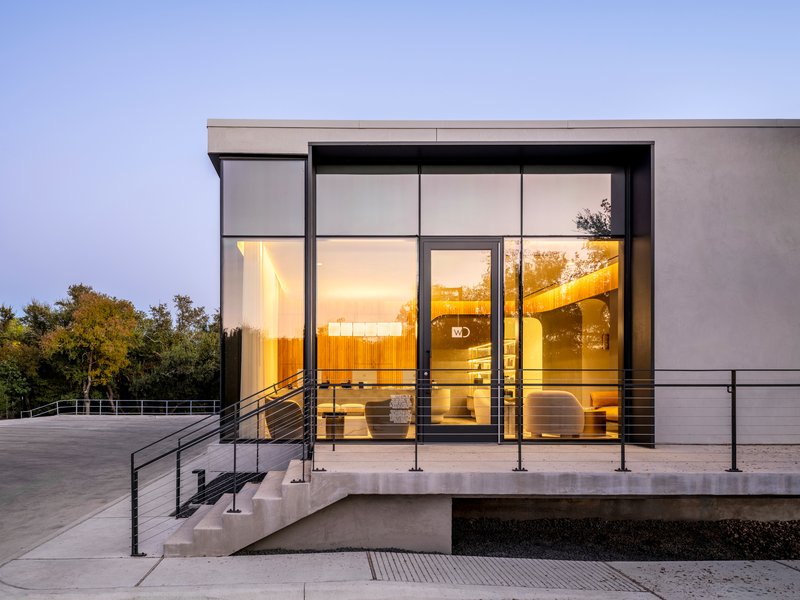 Glazed entrance at dusk showing illuminated interior with timber wall and floating sculptural pendant