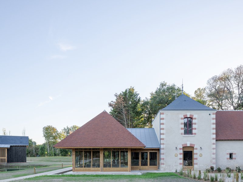 Glazed pavilion with pyramidal tile roof next to a rendered tower with brick quoins at dusk