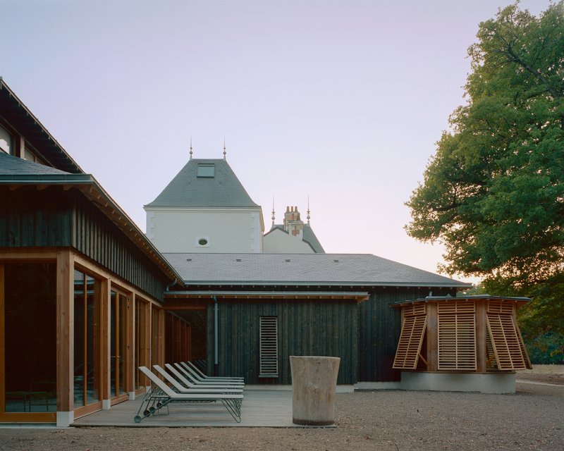 Gravel courtyard with striped lounge chairs and timber-slatted shutters beside dark vertical cladding