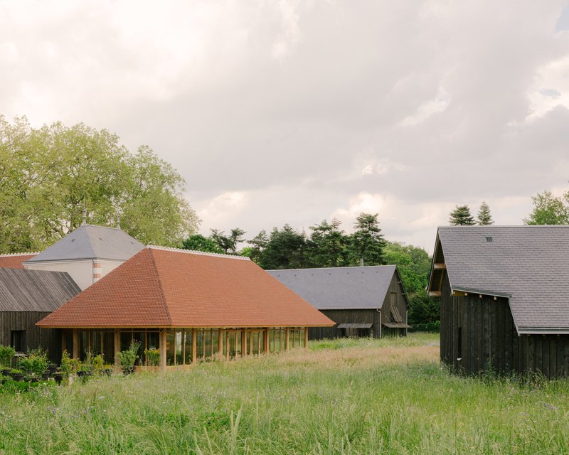 Low-pitched pyramidal roof with terracotta tiles rising above a grassy meadow and surrounding farm buildings