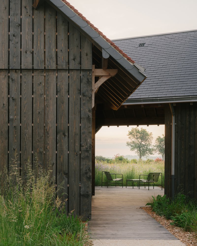 Timber-clad passageway framing a view of green chairs and wildflower meadow beyond