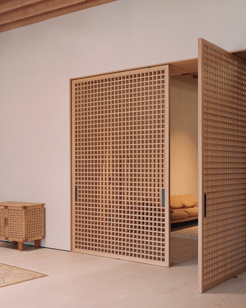 Close-up of a tall timber lattice screen with visible bedroom space beyond a narrow opening in the white wall