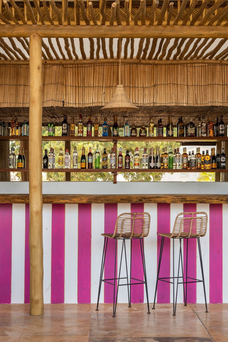 Bar counter with pink and white vertical striped front panel under bamboo ceiling with exposed timber structure