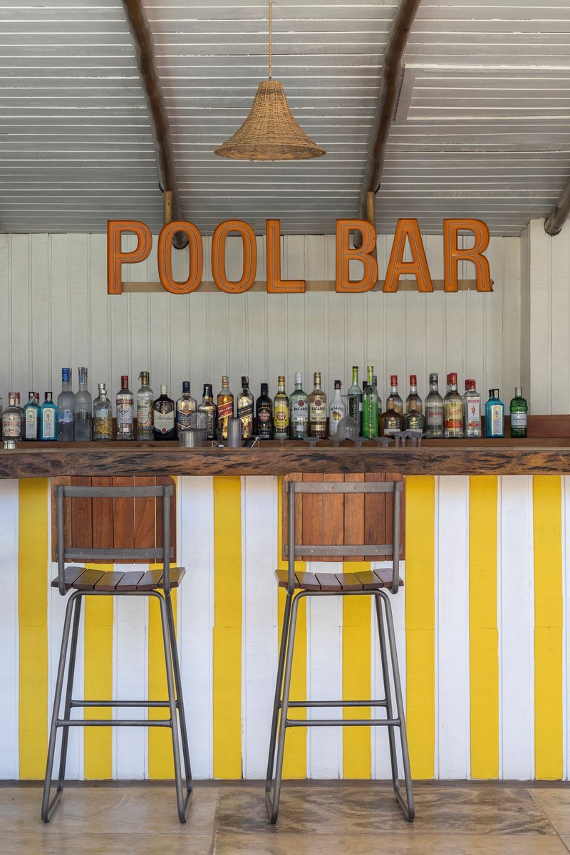Bar counter with yellow and white vertical striped front panel beneath metal stools and woven pendant light