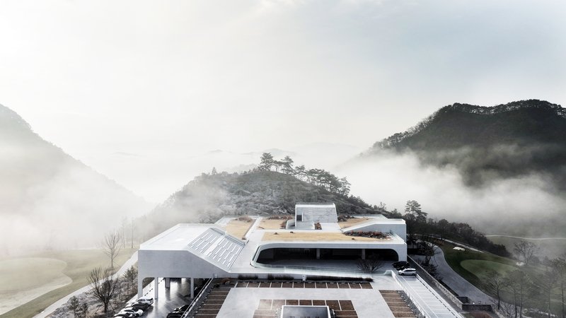 The layered building with curved rooflines and vegetated terraces surrounded by morning mist in the valley
