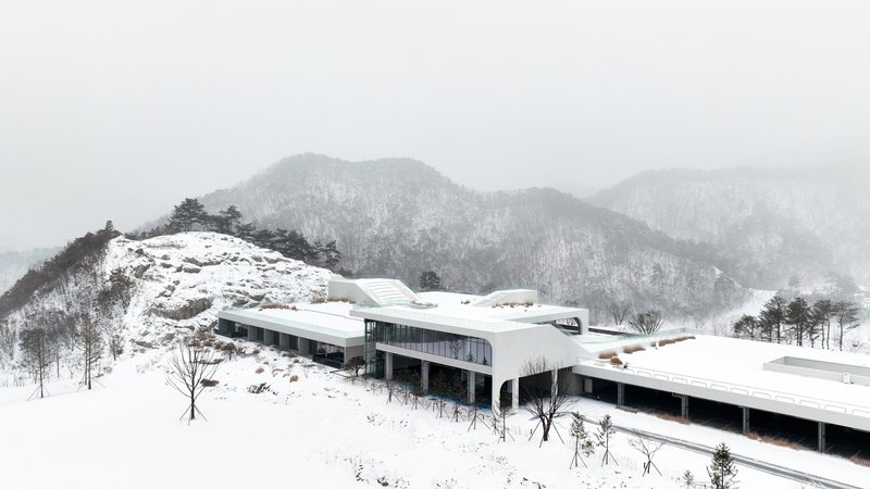 Winter view of the horizontal wings with glazed facades and white roofs stretching across the snowy hillside