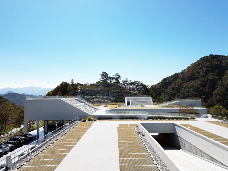 Rooftop view showing white volumes with planted gravel beds nestled into a forested hillside under clear blue sky