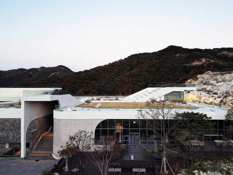 Curved entry canopy with timber staircase and glazed pavilion below white roof volumes at dusk