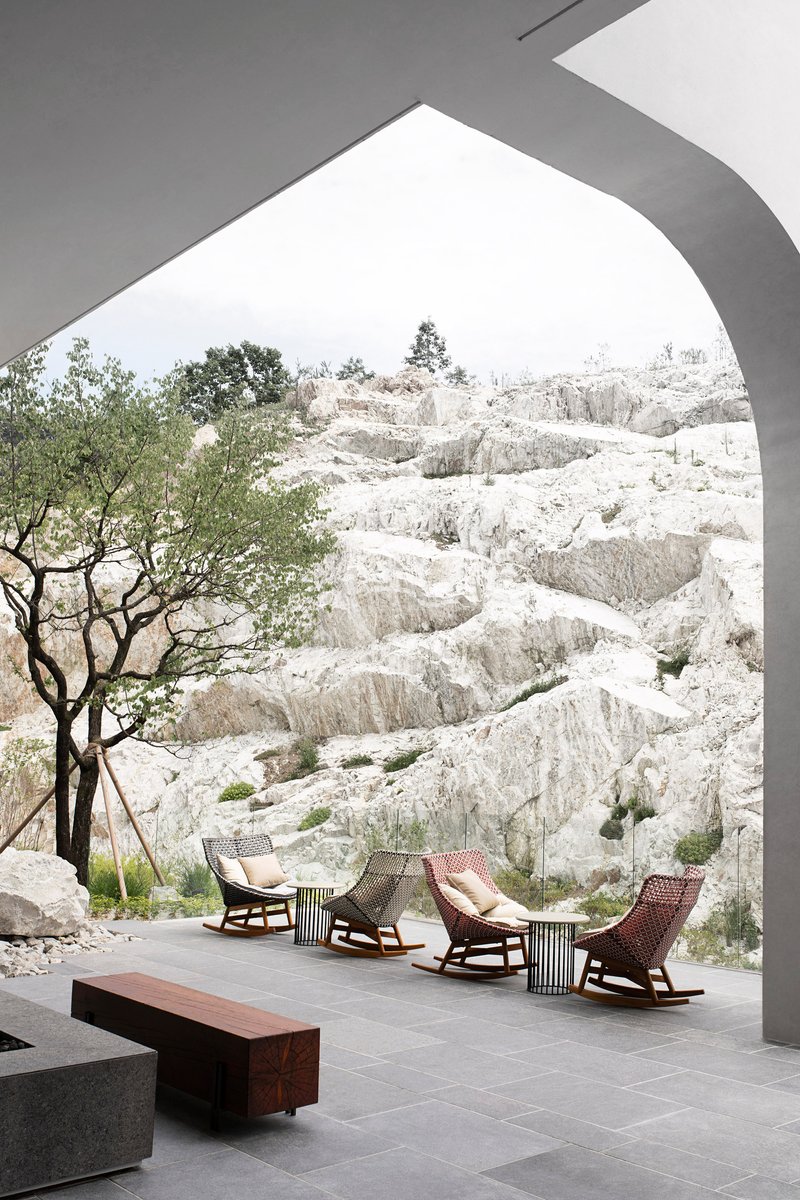 Covered terrace with woven rocking chairs framing a view of white limestone cliffs and a tree
