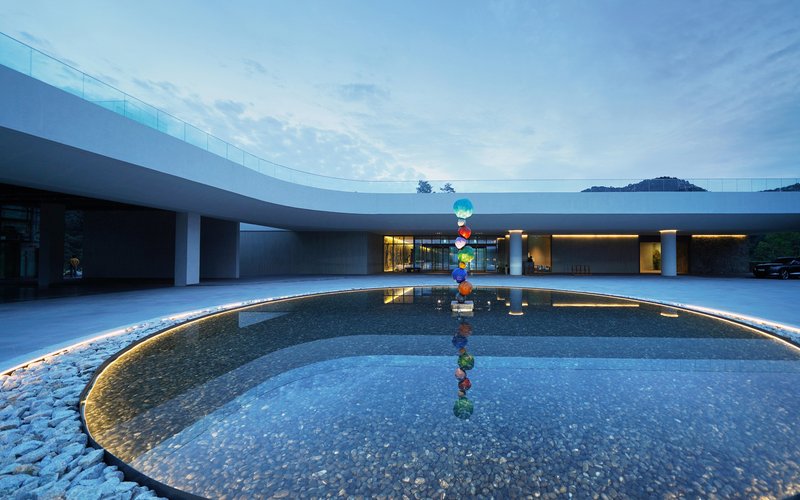 Curved courtyard pool with sculptural installation reflecting the glazed colonnade and mountains beyond at twilight