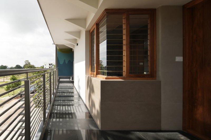 Covered balcony with horizontal metal railing creating striped shadow patterns on the tiled floor