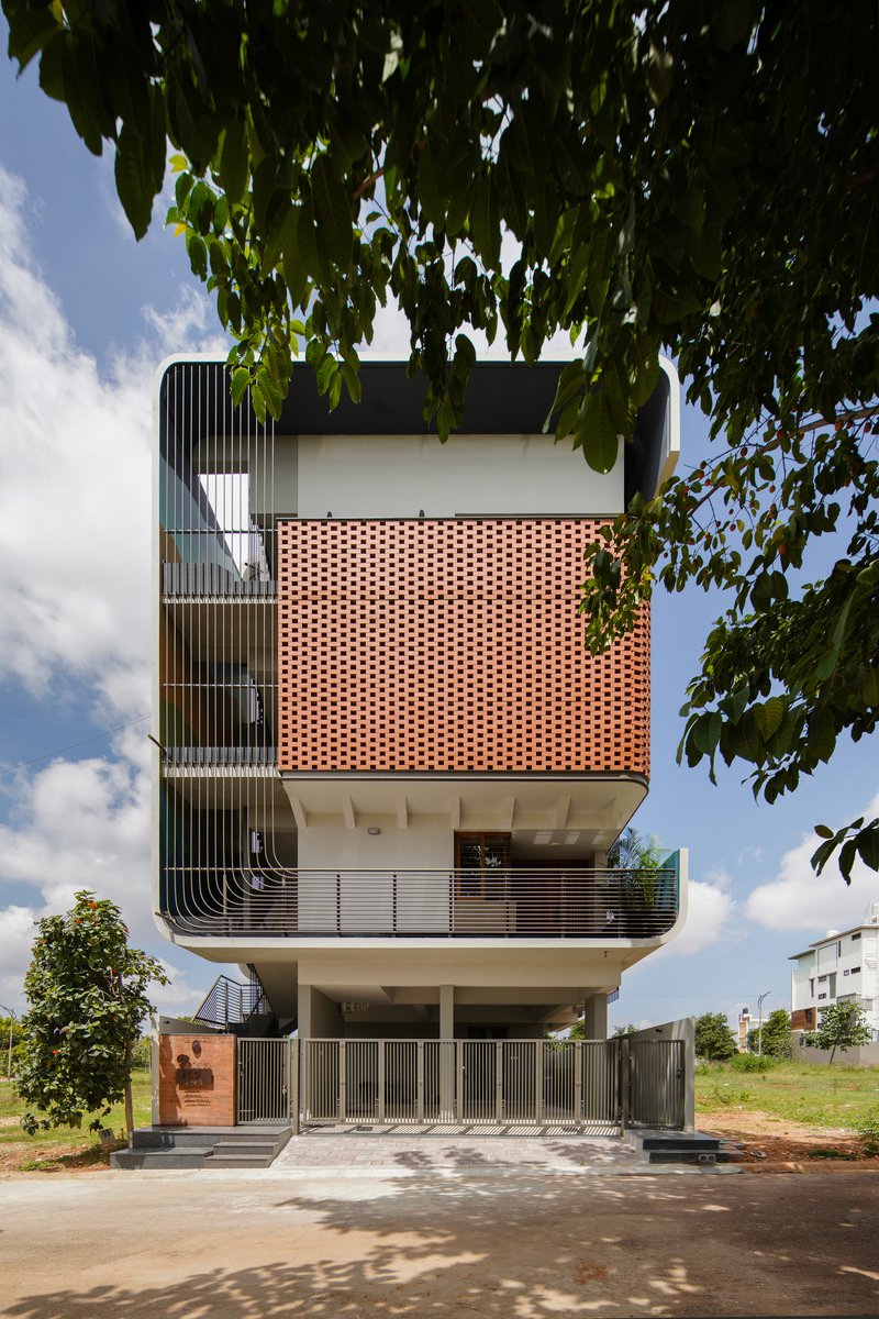 Front elevation showing vertical louver panels on the left and a perforated terracotta volume under afternoon clouds