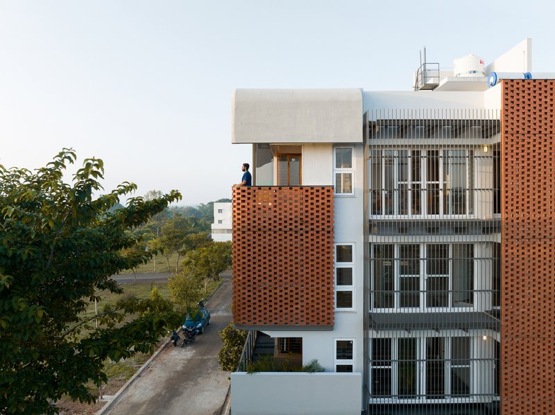 Street view showing the layered facade with a figure on the rooftop terrace at dusk