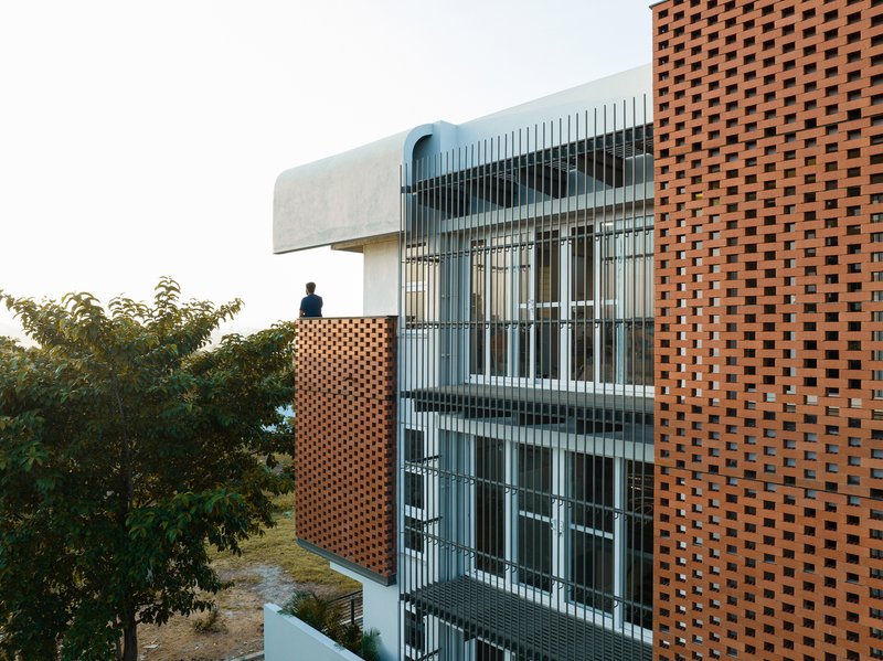 Close-up of the perforated brick panel and vertical metal screen facade with a figure on the balcony