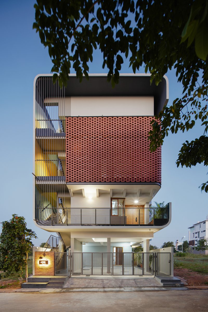 Street elevation showing the stacked volumes with perforated terracotta brickwork screen and cantilevered balconies at dusk