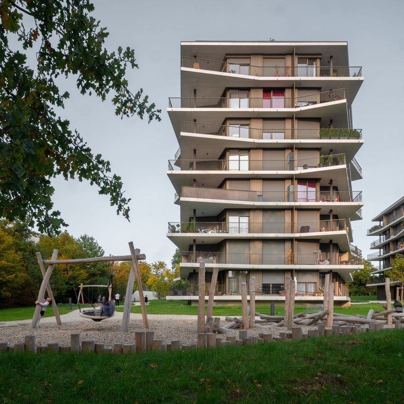 Tower facade with cantilevered concrete floor plates and timber balustrades above a playground with wooden logs