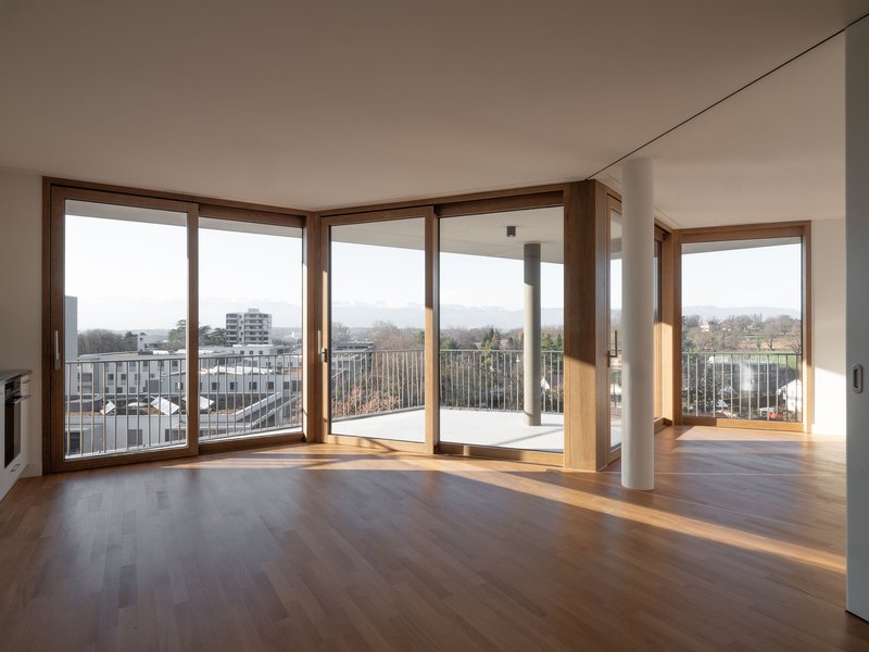 Timber-framed corner windows opening onto a terrace with oak flooring and a cylindrical column