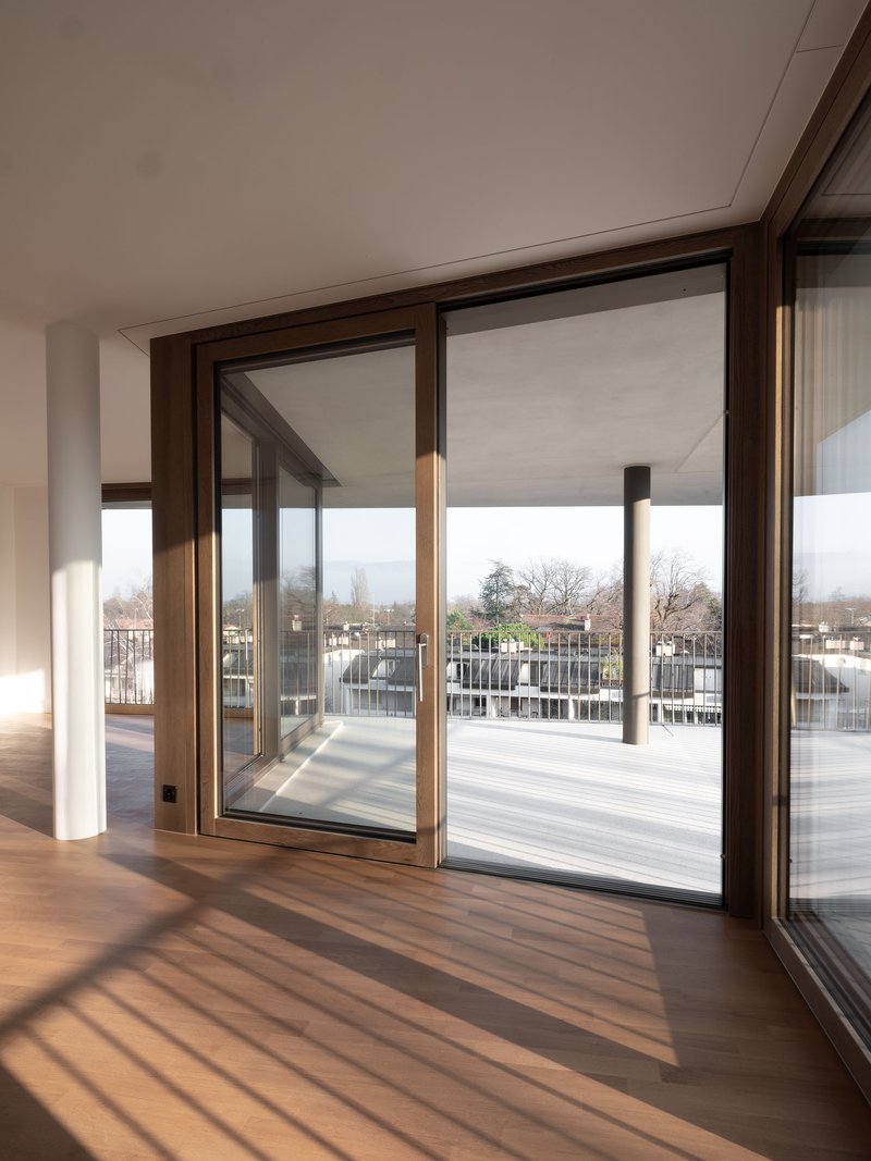 Interior view through bronze-framed sliding doors opening to a terrace with strong diagonal shadows on timber flooring