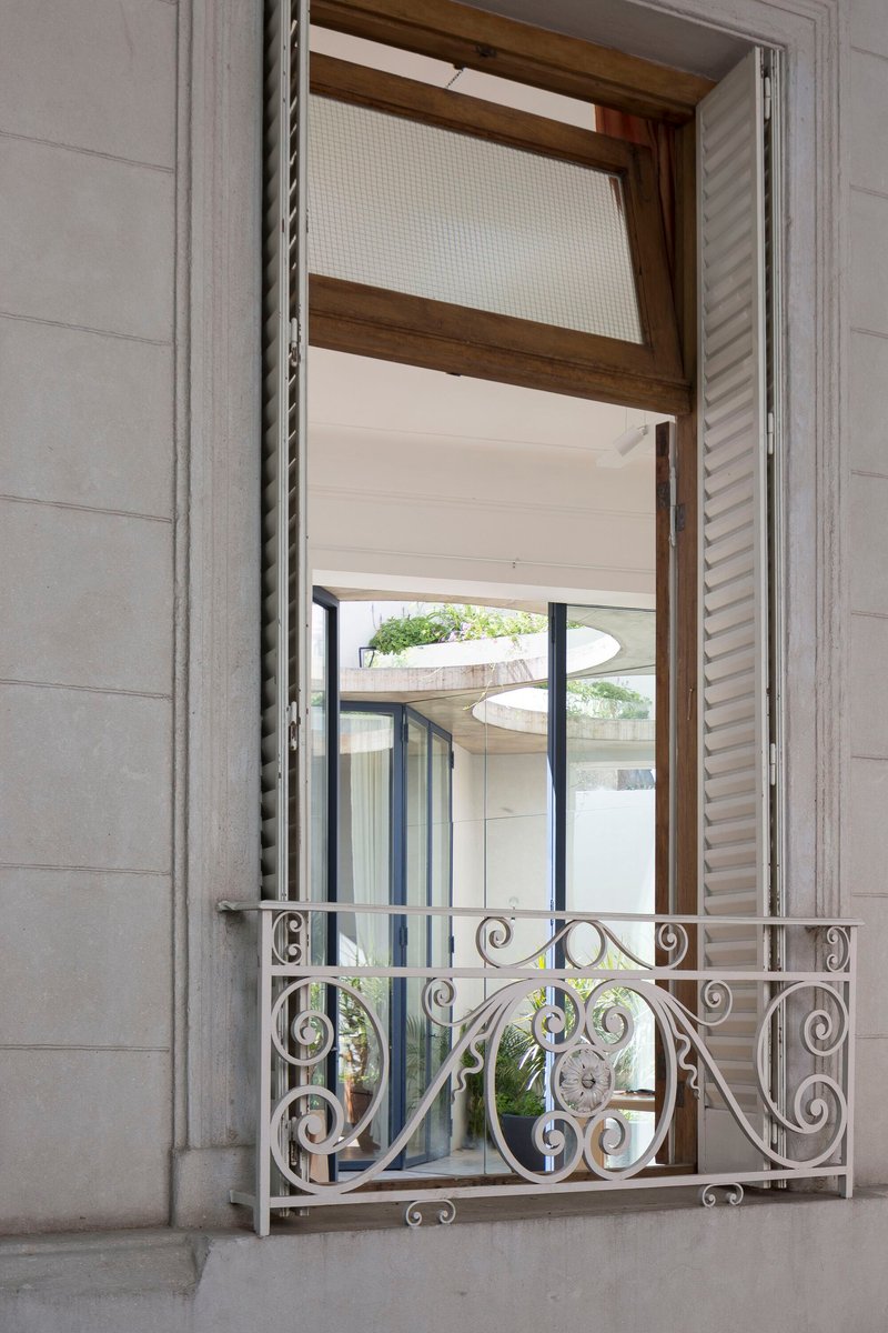 Open window with ornamental wrought iron balcony railing and timber frame looking into a planted courtyard