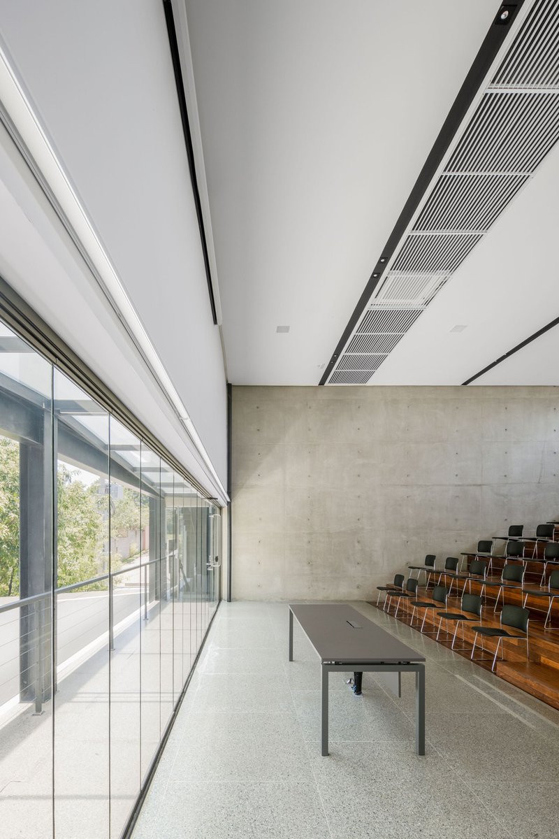 Interior assembly space with floor-to-ceiling glass wall, concrete backdrop and tiered wooden seating