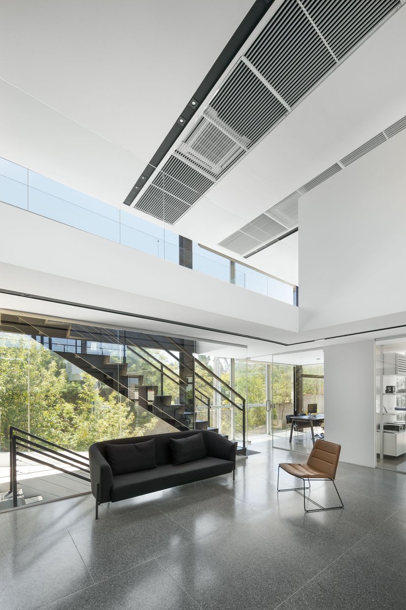 Double-height lobby with diagonal staircase, terrazzo flooring and linear ceiling grilles above