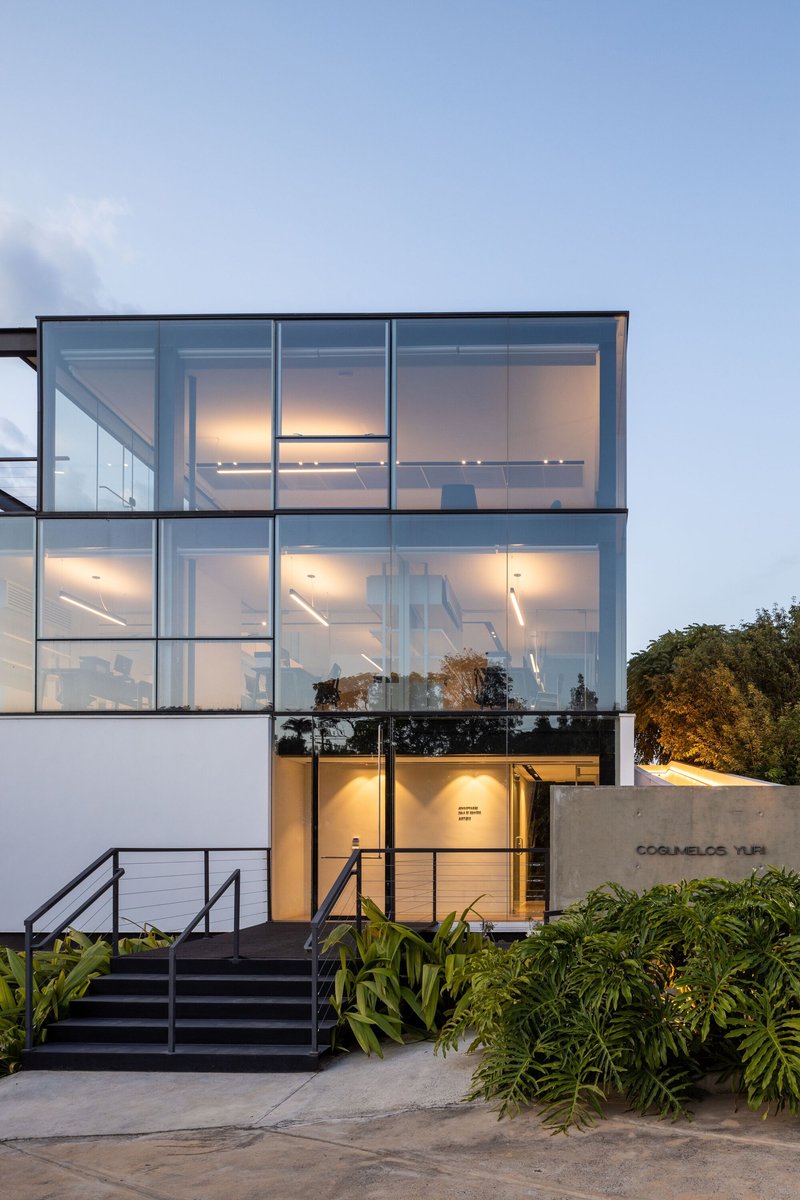 Three-story glass facade with exposed steel frame and interior lighting at dusk