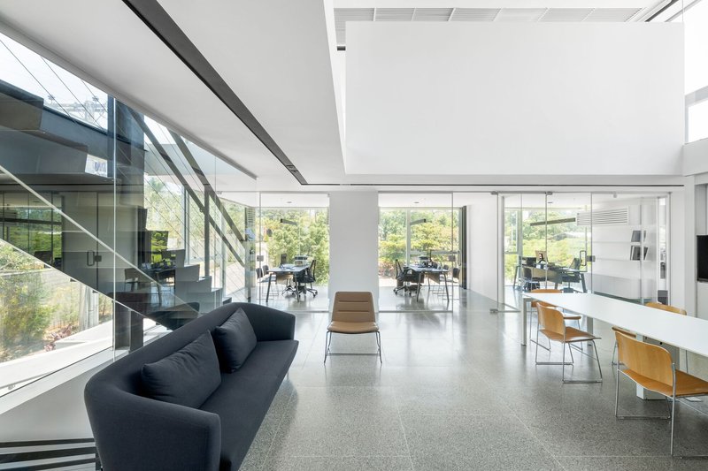 Open-plan workspace with full-height glazing overlooking gardens and a glass-walled staircase at left