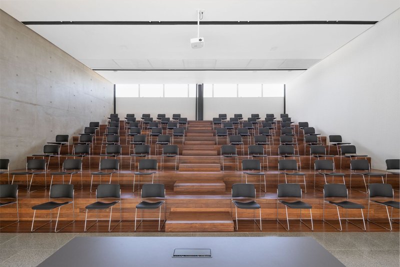 Frontal view of raked timber seating tiers and concrete walls lit by high clerestory glazing
