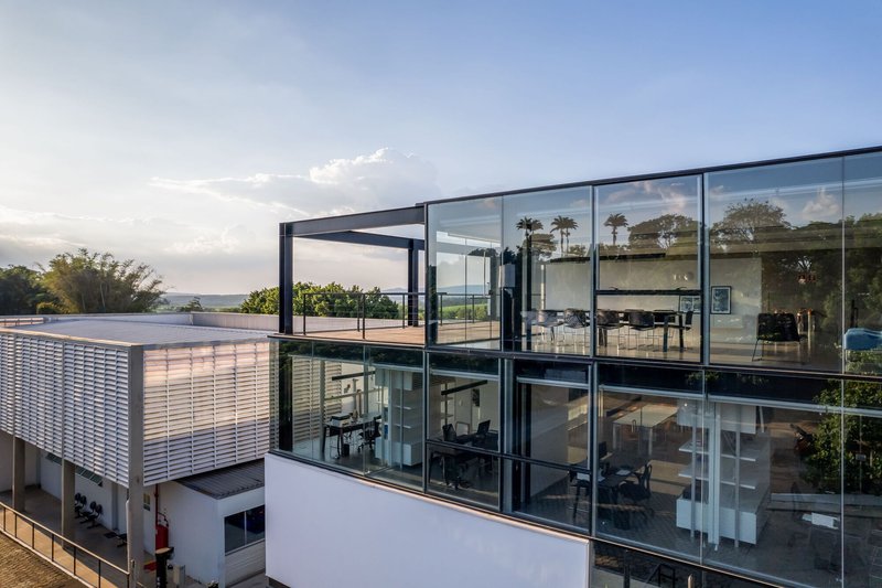 Upper level view of the glazed steel frame volume with louvered walls and palm trees beyond