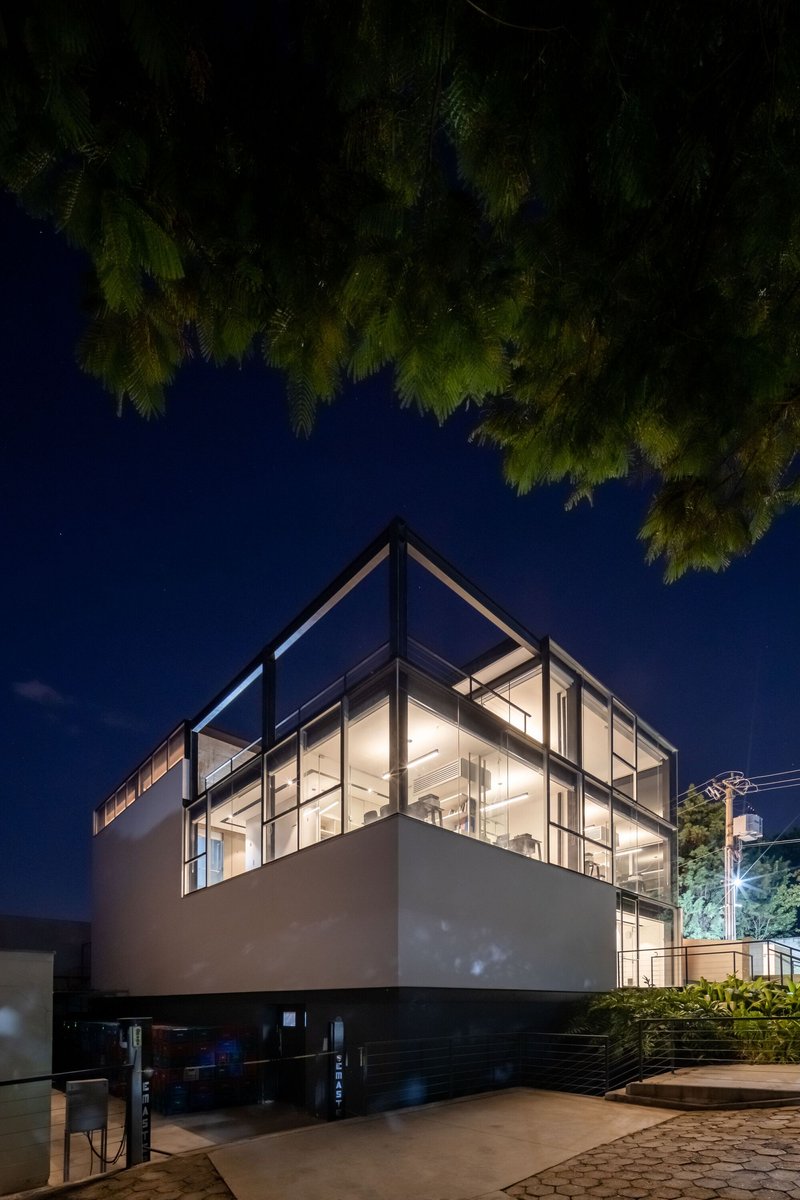 Night view of the glazed steel frame building glowing beneath overhanging tree branches