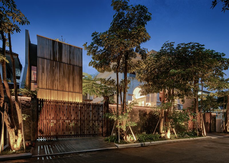 Street view of the timber facade and vertical slat fence screened by trees at dusk