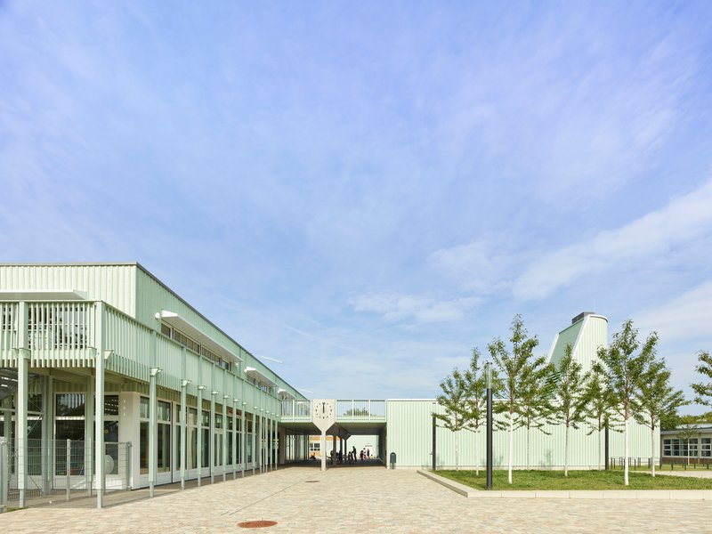 Courtyard view with corrugated metal facade and colonnade framing a passage under blue sky
