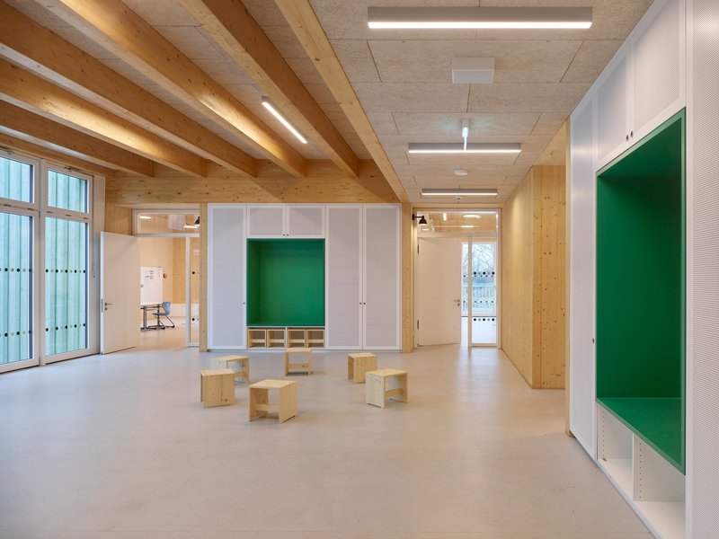 Interior classroom space with exposed timber beam ceiling and white storage cubbies flanking plywood benches
