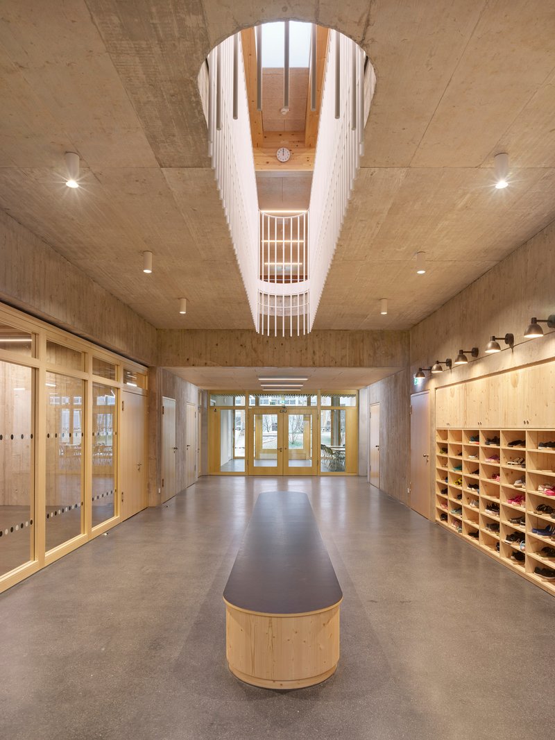 Entry corridor with central timber bench, concrete ceiling, and tiered lightwell opening above