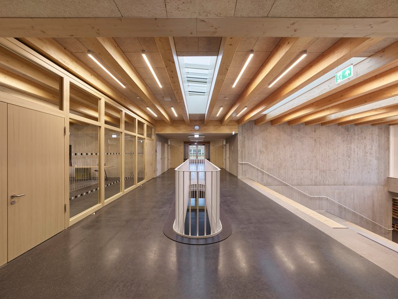 Corridor with exposed timber joists overhead and a cylindrical lightwell enclosure below