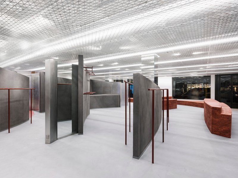 Open floor plan with freestanding grey partitions and copper handrails between concrete columns and white flooring