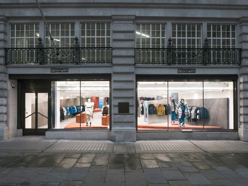 Street facade showing twin storefronts with large glazing below ornamental balconies on grey stone building