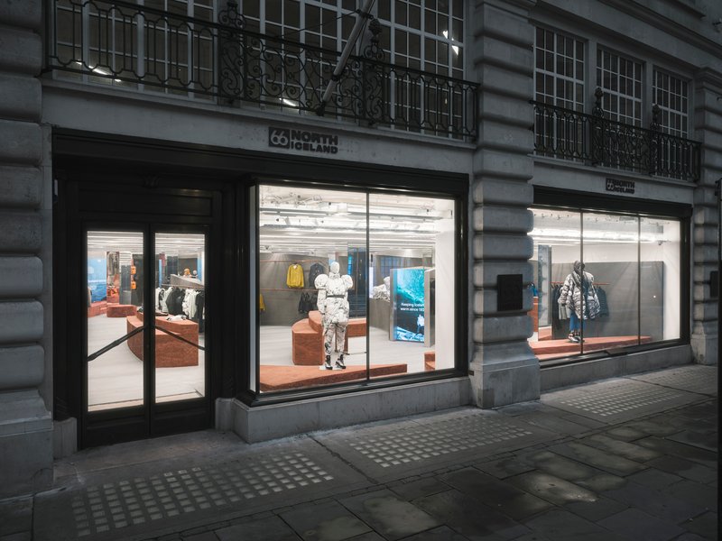 Evening view of symmetrical storefronts with illuminated interiors and mannequins beneath wrought iron balconies