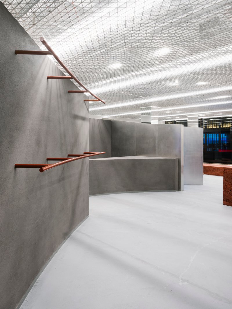 Copper-toned metal handrails extending from grey concrete walls beneath an expanded metal grid ceiling