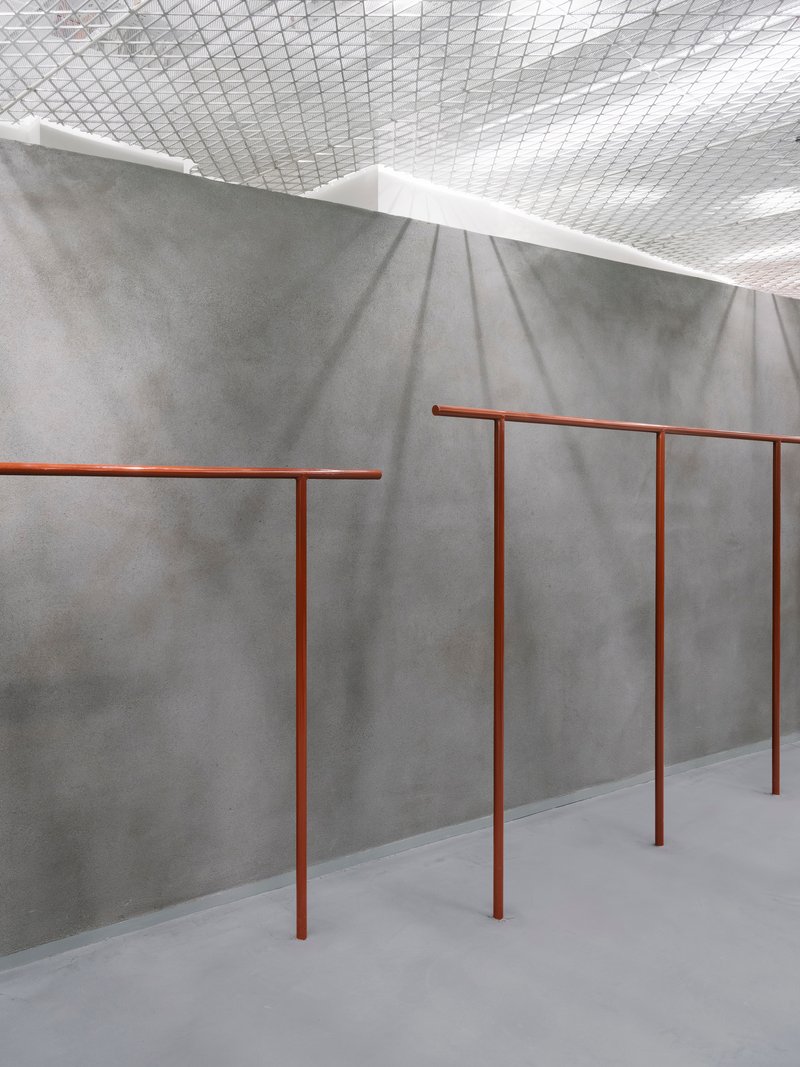 Close-up of copper-toned tubular railings against a folded grey concrete wall catching soft shadows