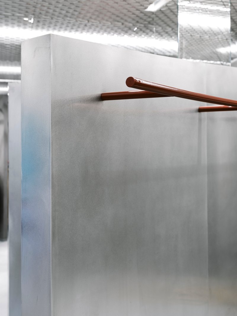 Close-up of a copper handrail extending from a grey concrete partition under diffused ceiling light