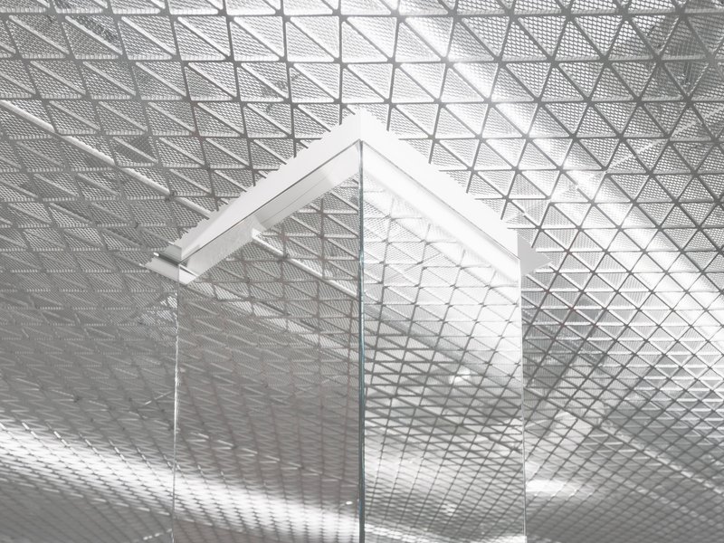 Glass corner panel set against the triangulated mesh ceiling with reflected light patterns