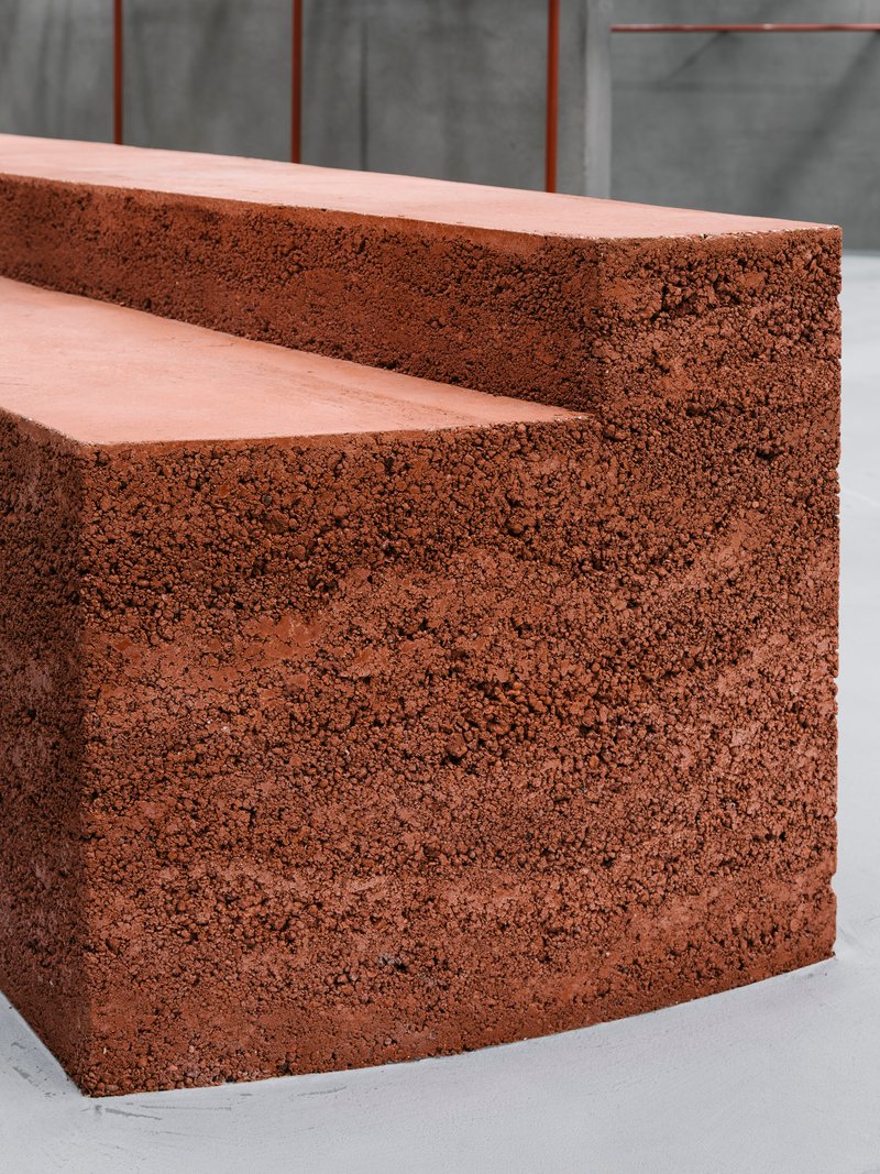 Close-up of reddish porous aggregate steps with smooth tread surfaces against a grey concrete backdrop