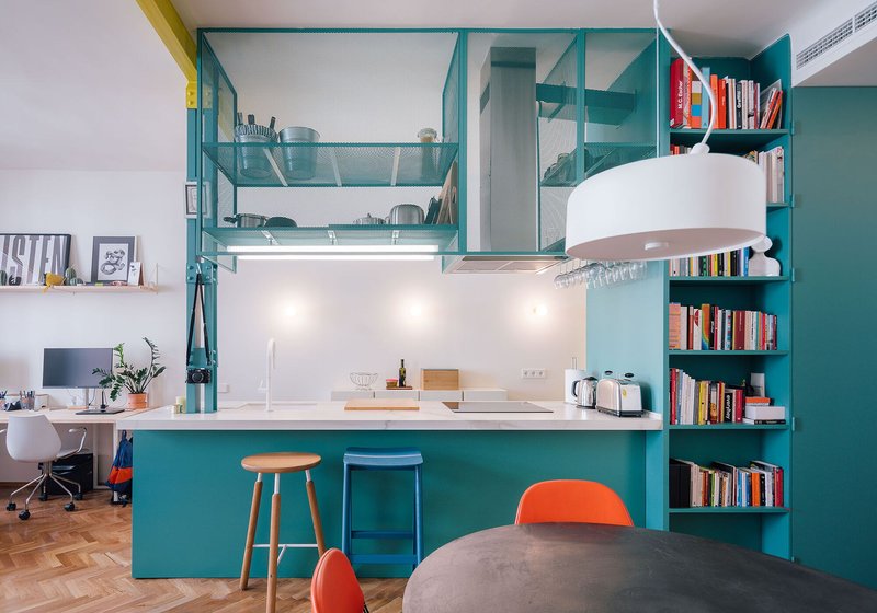 Kitchen counter with teal base cabinets, perforated upper storage, and under-cabinet lighting beside work desk