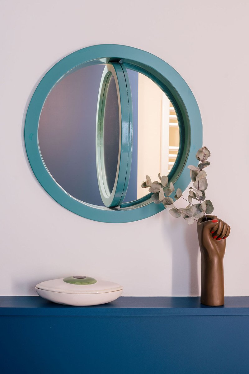 Teal circular mirror above a blue counter with dried eucalyptus in a wooden vase