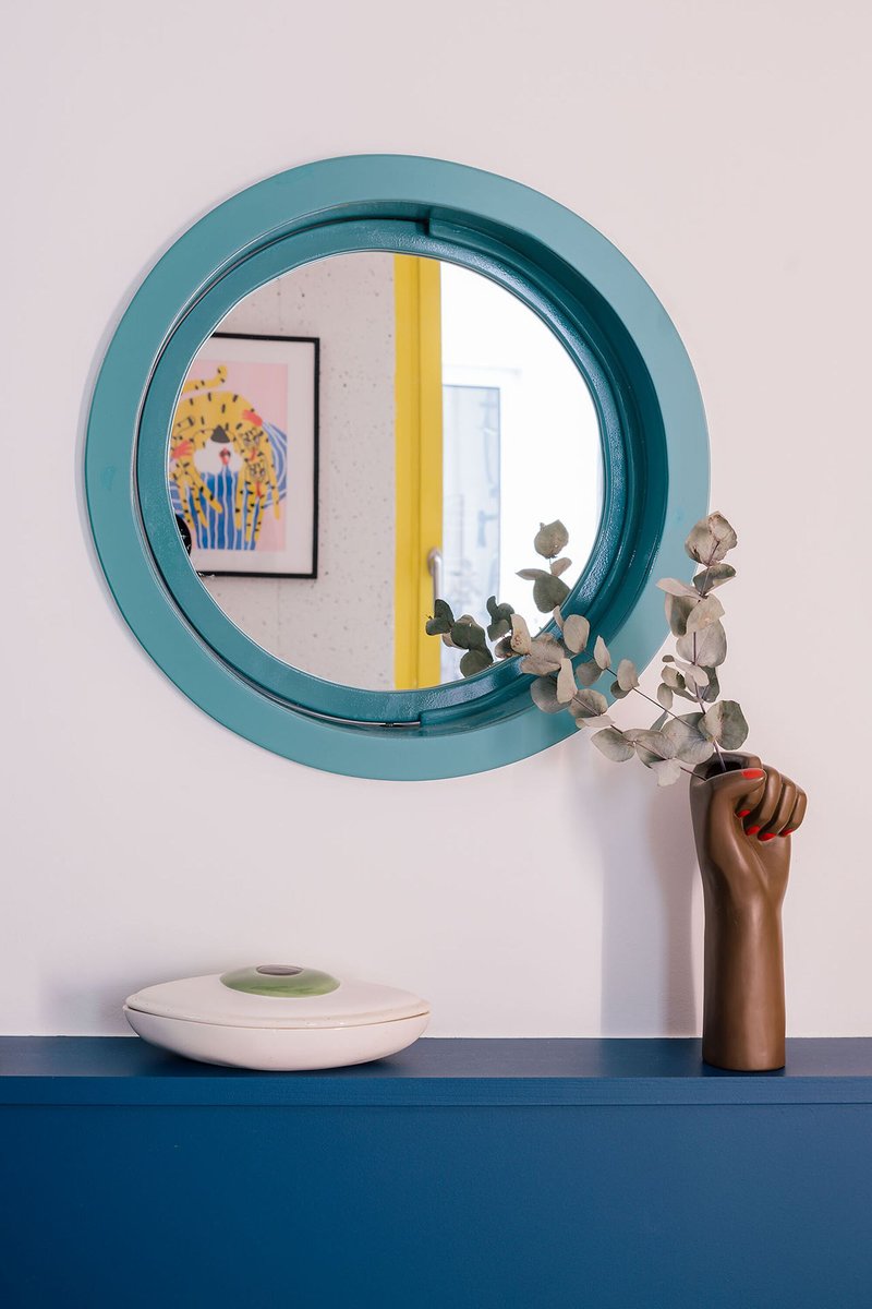 Reflection in teal circular mirror showing yellow door trim and framed artwork on the wall