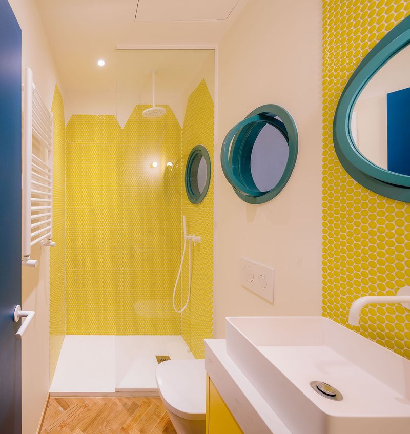 Bathroom with yellow penny tile shower enclosure and teal porthole mirrors flanking white vanity
